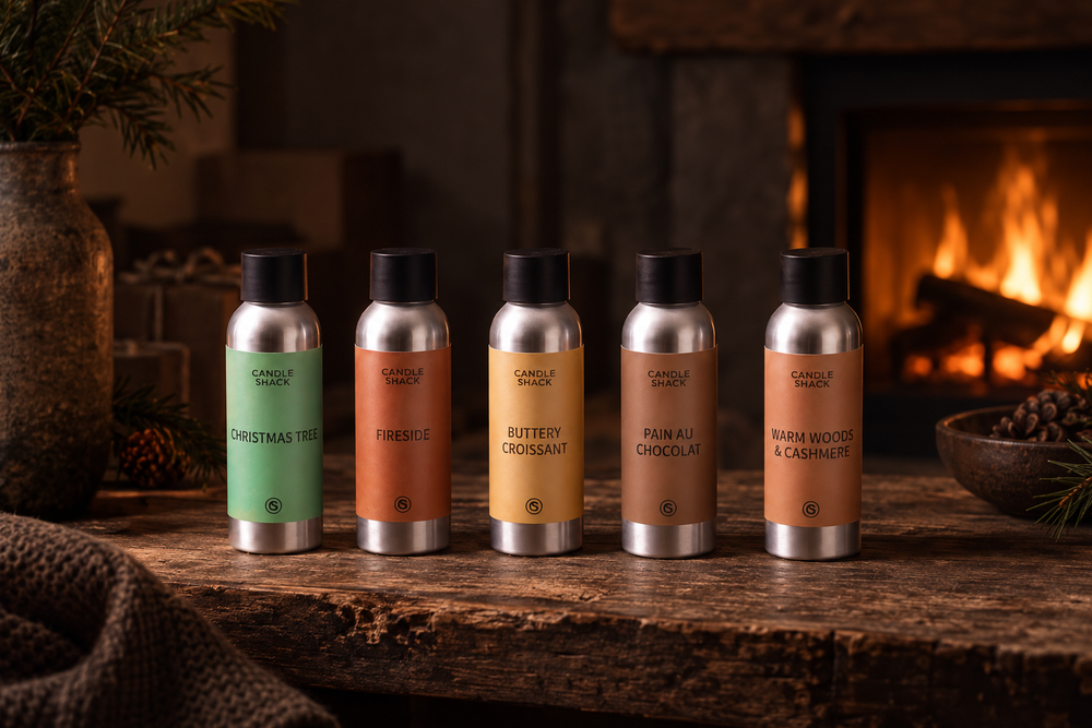 Five Candle Shack fragrance oil bottles - Christmas Tree, Fireside, Buttery Croissant, Pain au Chocolat and Warm Woods & Cashmere - by a fireplace.