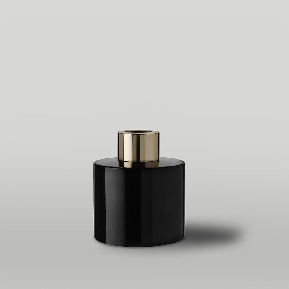 Black gloss diffuser bottle with a gold lid on a light gray background