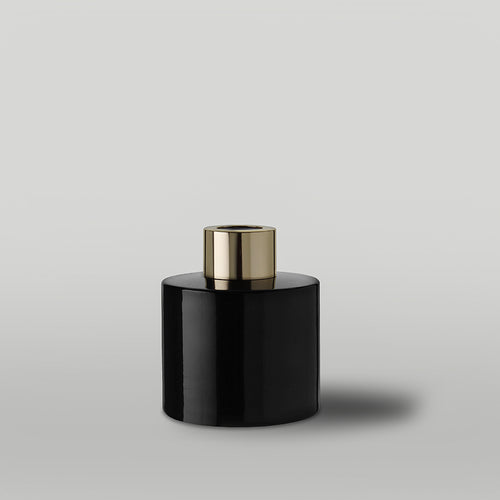 Black gloss diffuser bottle with a gold lid on a light gray background