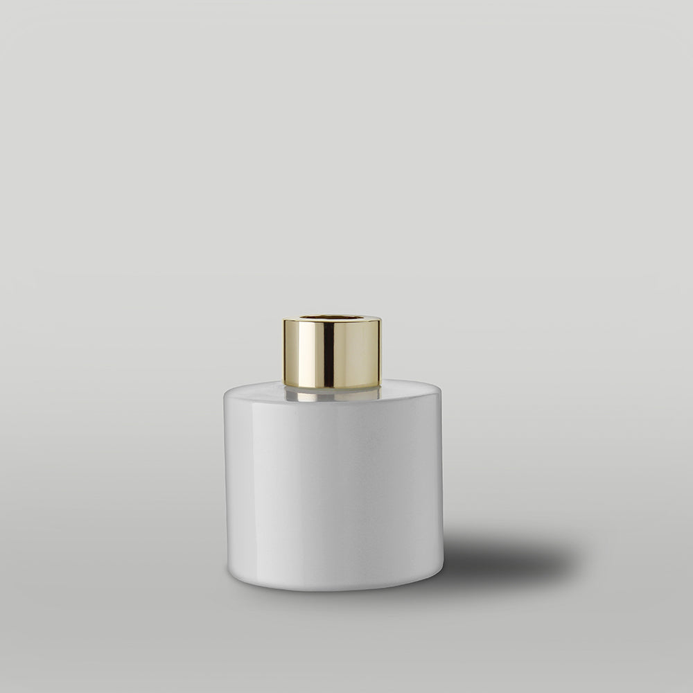 Gloss white diffuser bottle with a gold cap on a light grey background