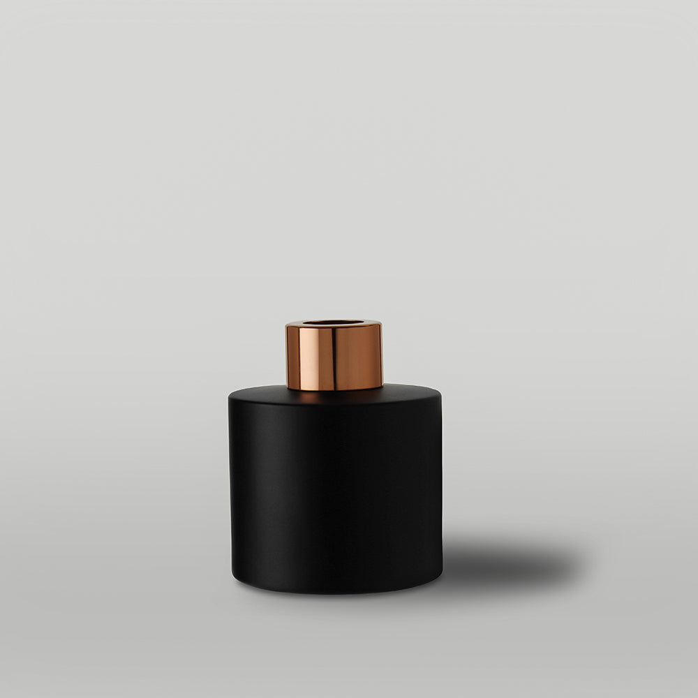 Black diffuser bottle with a copper top on a light gray background