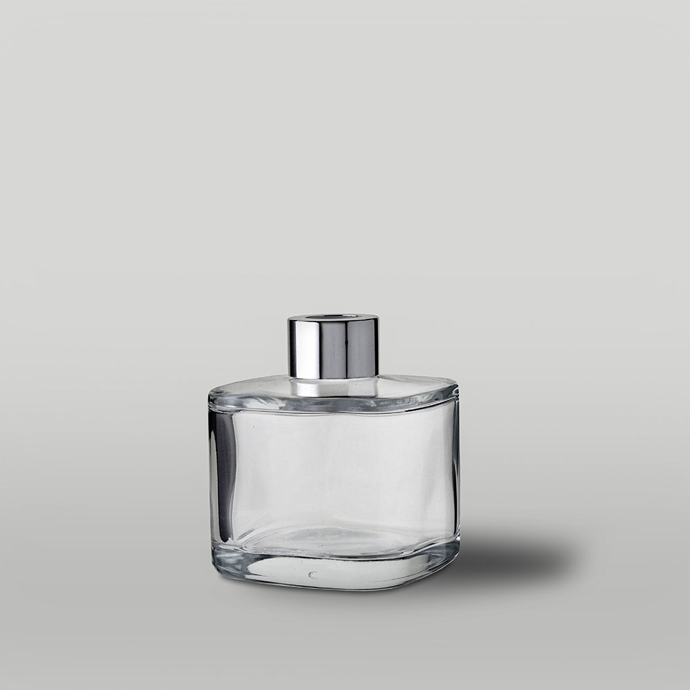 Clear glass diffuser bottle with silver cap on a gray background