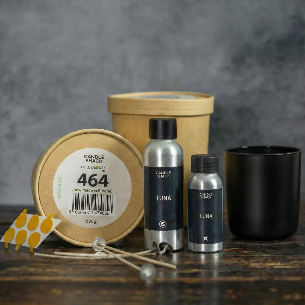 Candle-making kits including tins, bottles, and candle jars on a wooden surface with a grey background.