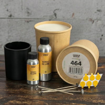 Candle-making kit including containers, wicks, and wax on a wooden surface with a grey brick wall background.