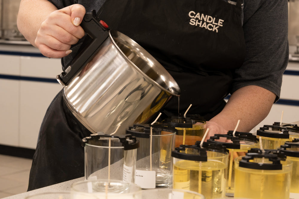 Person in a Candle Shack apron pouring liquid into small containers.