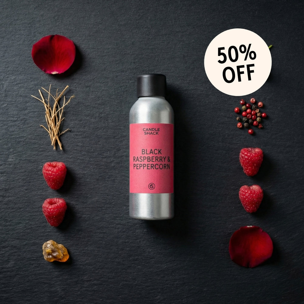 Candle with black raspberry and peppercorn fragrance oil on a dark surface with raspberries and rose petals.