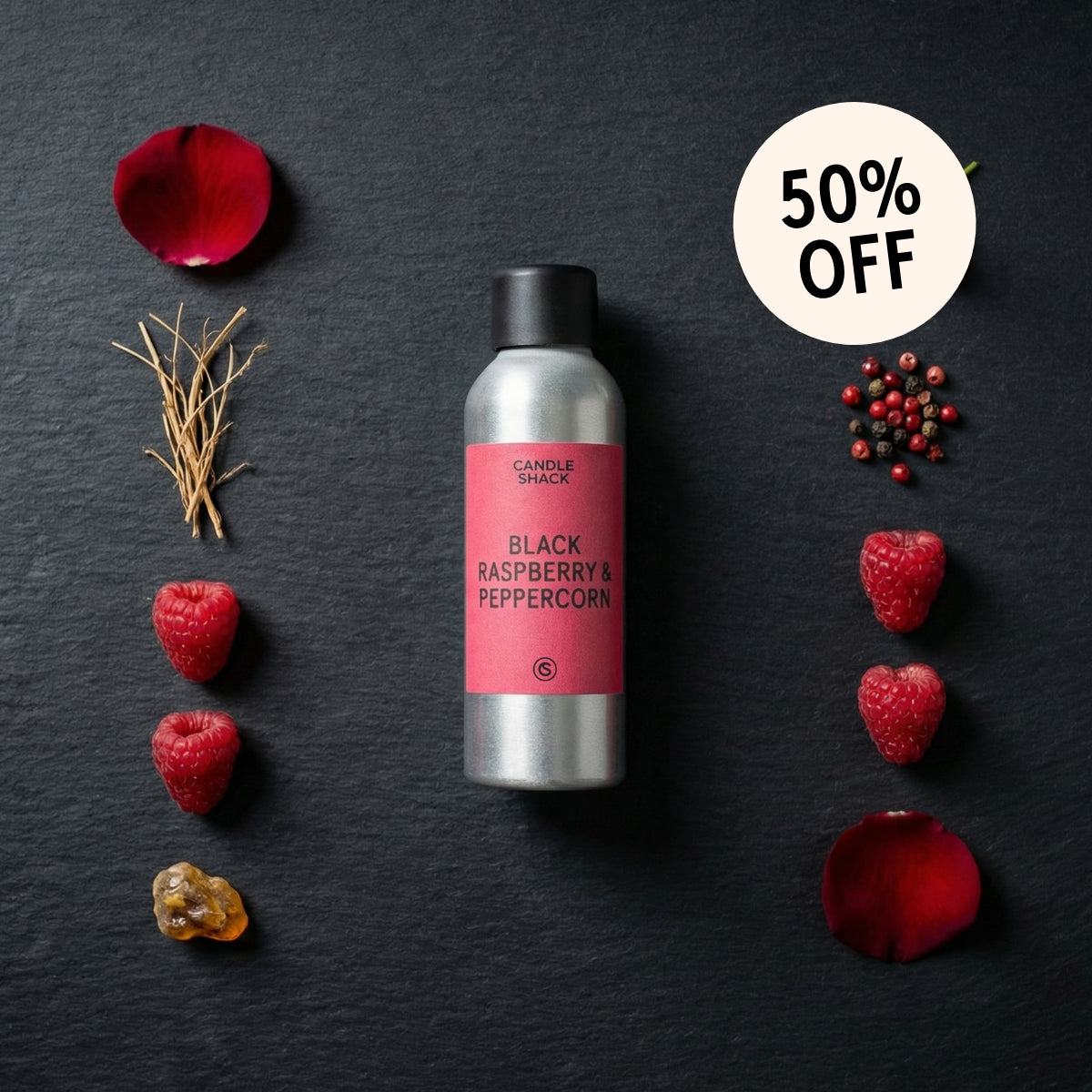 Candle with black raspberry and peppercorn fragrance oil on a dark surface with raspberries and rose petals.