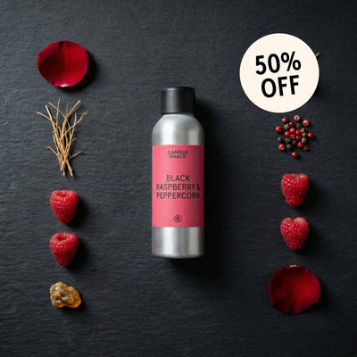 Candle with black raspberry and peppercorn fragrance oil on a dark surface with raspberries and rose petals.