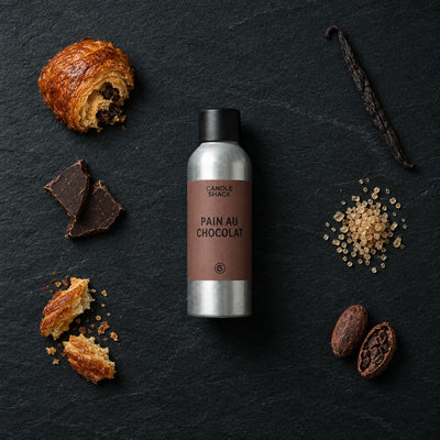 Pain Au Chocolat fragrance oil - Candle Shack aluminium bottle with dried botanicals on a dark slate background