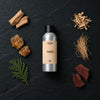 Tamed fragrance oil - Candle Shack aluminium bottle with dried botanicals on a dark slate background
