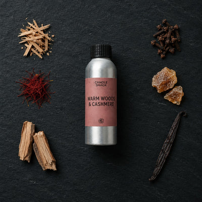 Warm Woods & Cashmere fragrance oil - Candle Shack aluminium bottle with dried botanicals on a dark slate background