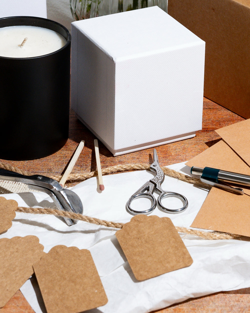 Candle making supplies, white box, scissors, and brown paper on a wooden surface
